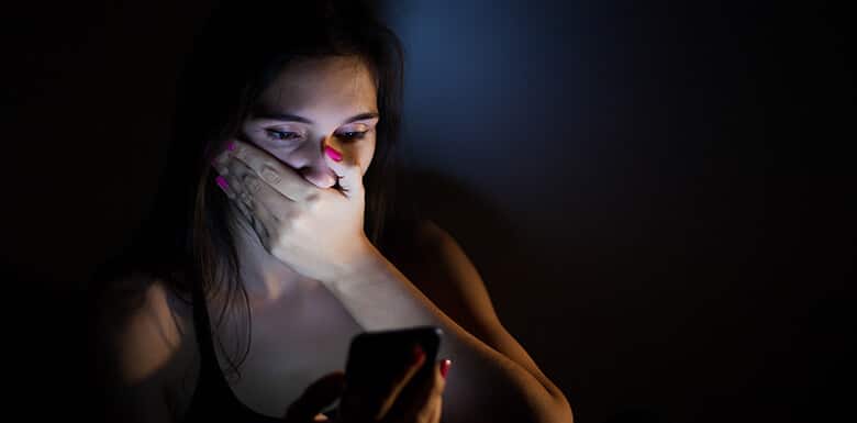 Woman sitting in the dark while looking at phone