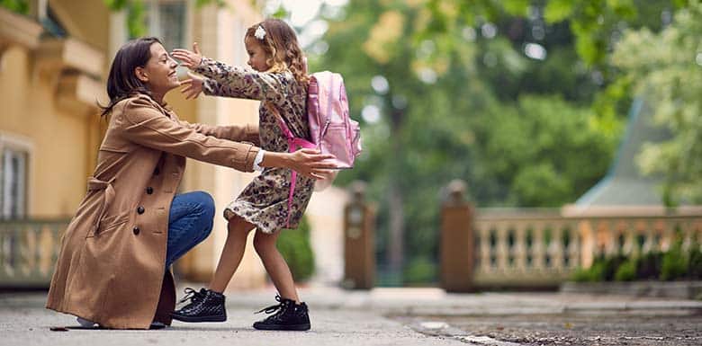 Woman bending down to hug daughter after school