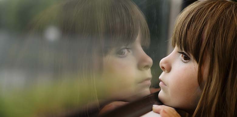 Young girl sitting close to window staring out the glass
