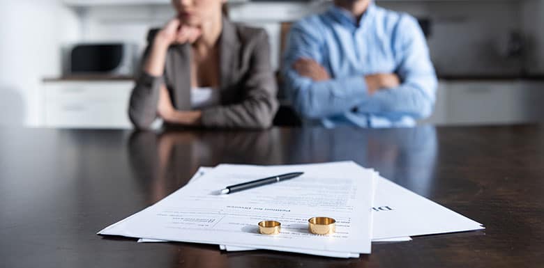 Woman and Man sitting next to each other with arms folded. Papers with wedding bands in front of them