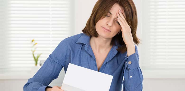 Woman holding forehead while looking at paper