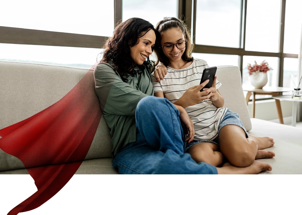 Mother sitting with daughter on couch looking at cellphone together, graphic overlay of hero cape on mother