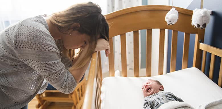 Mom leaning against baby crib while baby cries
