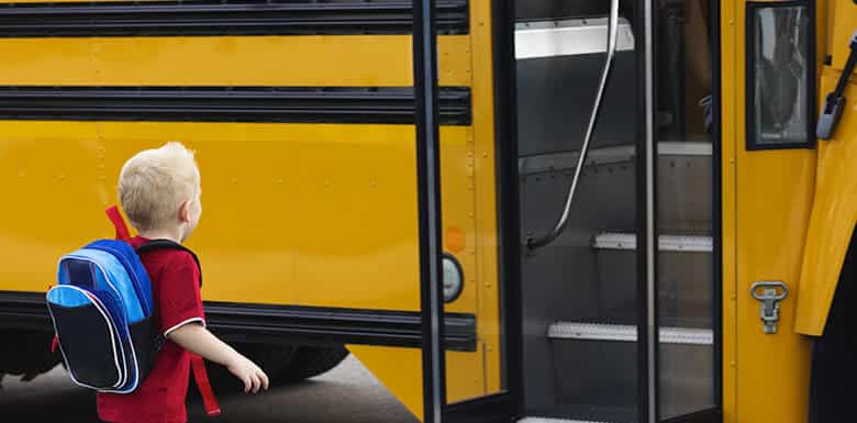 Young boy with book bag getting onto school bus