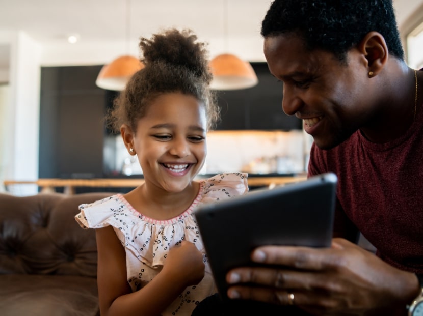 Dad and daughter sitting on couch together looking at iPad